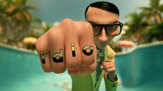 A man in glasses and a yellow suit holds a fist toward the camera with 'radio' written on his knuckles.
