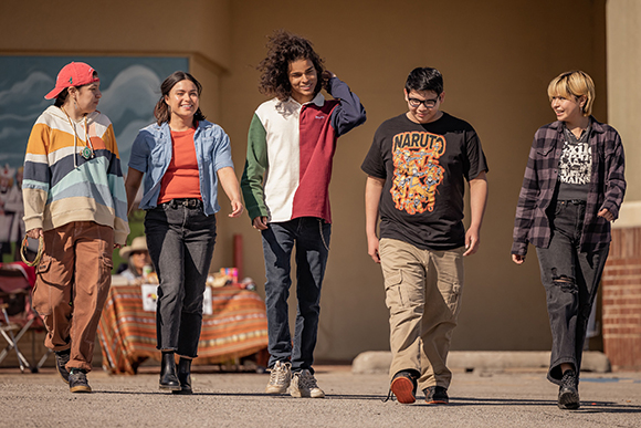 Five diverse young people walking side-by-side on a paved surface during the day.