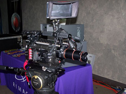 A professional cinema camera with a lens and monitor is mounted on a tripod, resting on a purple table.