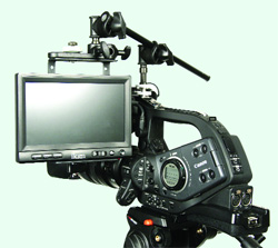A black professional video camera equipped with a large external monitor and various mounting accessories.