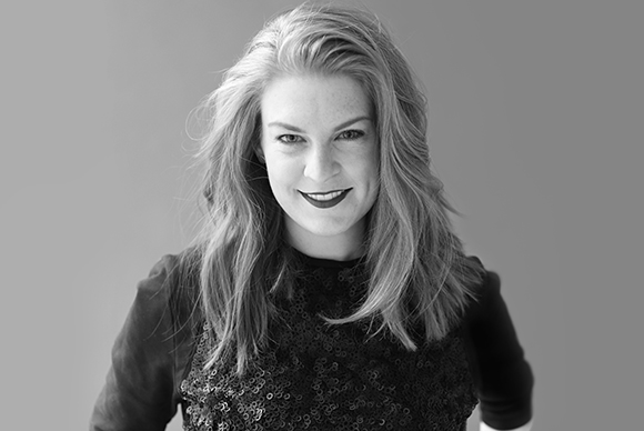 Black and white portrait of a smiling woman with long, wavy hair wearing a sequined top.
