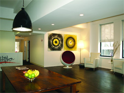 A modern living room featuring a wooden table, a white armchair, and two circular abstract paintings on the wall.