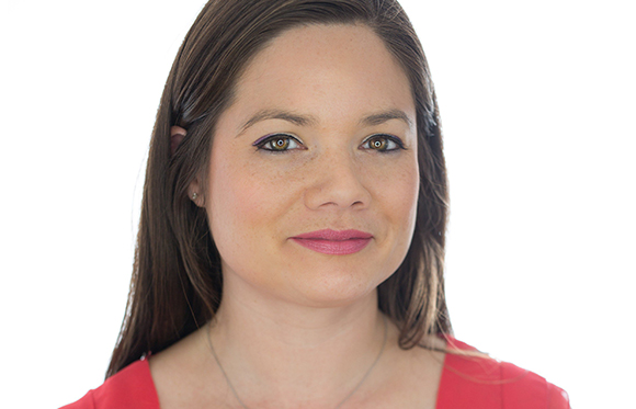 A woman with brown hair, green eyes, and pink lipstick looks forward against a white background.