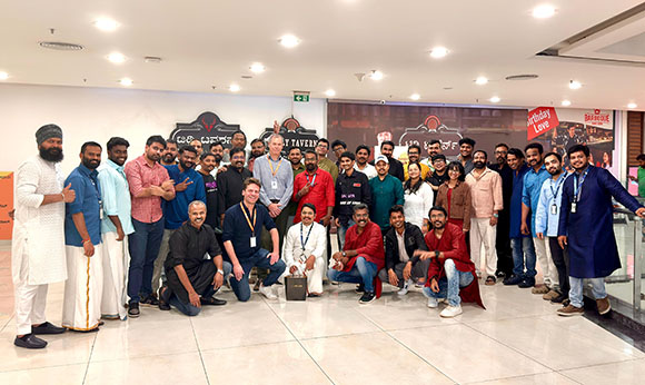 A large group of diverse people posing together in a bright, modern indoor hallway.
