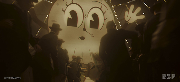 Silhouetted crowd facing a giant, smiling cartoon moon face illuminated by string lights.