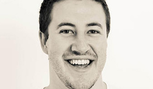 A close-up portrait of a smiling man with short dark hair against a white background.