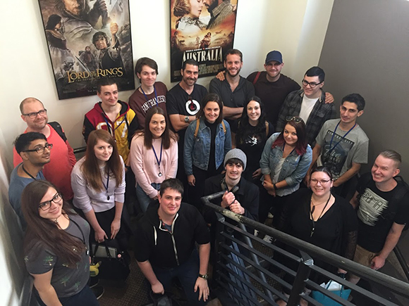 A large group of young adults posing together in a narrow indoor hallway.