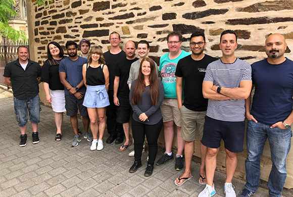 A diverse group of eleven adults posing for a group photo in front of a textured stone wall.