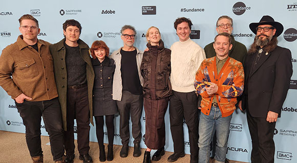 Ten people standing in a line posing for a group photo against a blue backdrop with various logos.