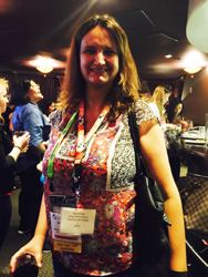 A woman with brown hair smiles, wearing a colorful blouse and a lanyard with multiple conference badges.