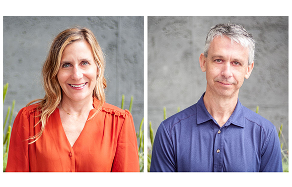 A woman in an orange blouse and a man in a blue polo shirt posing against a gray textured wall.