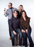 Four smiling adults posing together against a white background.
