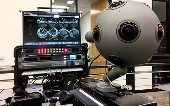 A large grey spherical camera with multiple lenses sits next to a monitor displaying spherical video feeds.