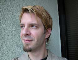 A man with short blonde hair and a goatee smiling slightly while looking off-camera.