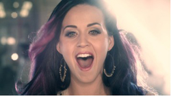 A woman with dark hair and purple highlights smiles broadly with her mouth open.