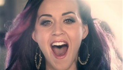 A woman with dark hair and purple highlights smiles broadly with her mouth open.