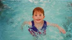 A young child with reddish hair swimming in a blue swimming pool.
