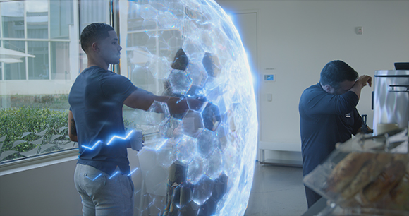 A man reaches out to touch a large, glowing blue holographic sphere in a bright office.