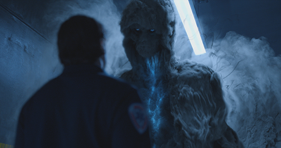 A person in silhouette faces a large, ethereal figure made of swirling blue smoke and light.
