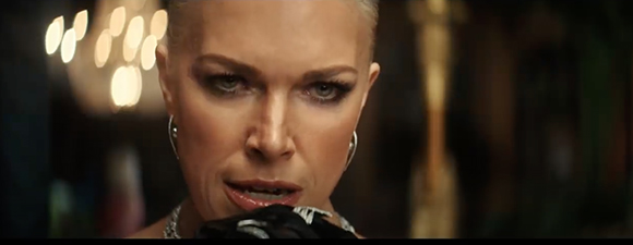 Close-up of a woman with dark eye makeup and silver earrings looking intensely forward.