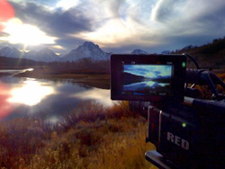 A digital camera screen displays a landscape of mountains and a lake during sunset.