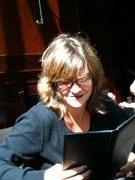 A woman with blonde hair and glasses looking down while reading a dark book.