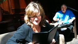 A woman with blonde hair and glasses reads a black book in a dark room.