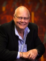 A smiling bald man wearing glasses, a black blazer, and a light blue button-down shirt.