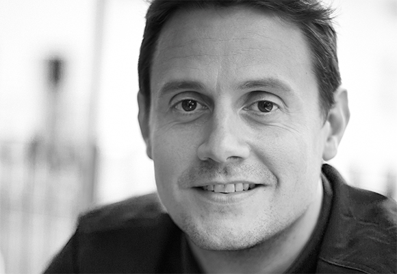 Black and white close-up portrait of a man smiling at the camera.