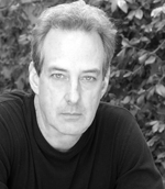 Black and white close-up portrait of a man with light-colored hair looking directly at the camera.