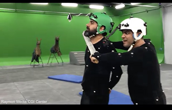 Two men in black motion capture suits and helmets pose in a green screen studio with props.