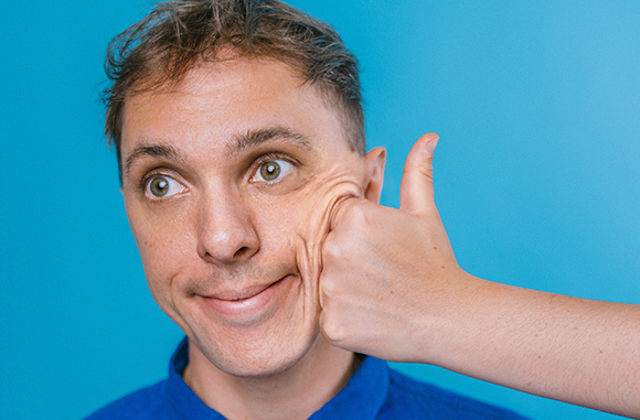 A man looks upward with a slight smile as a hand gives a thumbs up in front of his face.