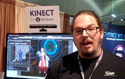 A man with glasses and a goatee stands before a monitor displaying software and a Kinect sign.