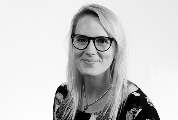 Black and white portrait of a smiling woman with long blonde hair and dark-rimmed glasses.