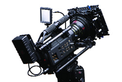 A complex professional cinema camera rig with a large lens and various attachments on a tripod.