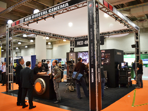 People gather around a Red Digital Cinema booth featuring cameras and large digital displays.