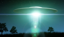A glowing saucer-shaped spacecraft hovering over a dark silhouette of trees and grass under a starry sky.
