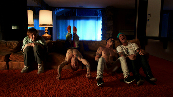 Four men posing in a dark living room with a red carpet and blue light from a window.