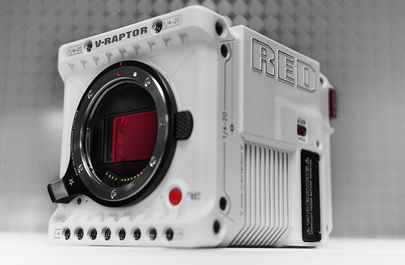 A white V-RAPTOR digital cinema camera shown from a side angle against a grey background.