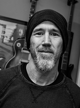 Black and white portrait of a man with a beard wearing a dark beanie and sweatshirt.