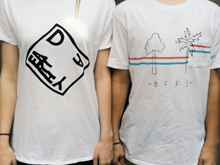 Two people standing side-by-side wearing white t-shirts with black line art graphics.