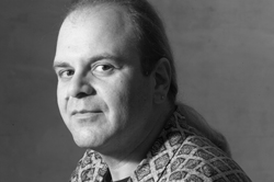 Black and white headshot of a man with light hair pulled back, wearing a patterned shirt.