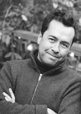 A man in a zip-up sweater smiling with his arms crossed in a black and white portrait.