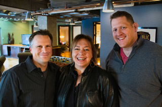 A man and a woman in the foreground and another man smiling in an indoor setting.