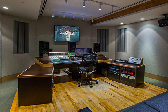 A professional recording studio featuring a large mixing console, studio monitors, and wooden flooring.