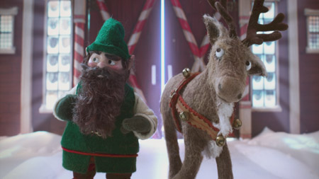 Felt puppets of a bearded elf in green and a reindeer standing in the snow.