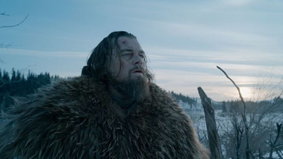 A man with long hair and a beard wearing a thick fur coat looks up against a wintry landscape.