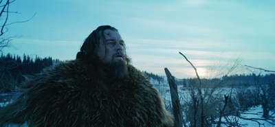 A man with a beard and long hair wearing a heavy fur coat stands in a snowy, wintry landscape.