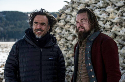 A man in a black puffer jacket and a man with a beard in a red period costume stand before a shell mound.