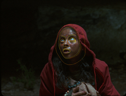 A person wearing a red hood with yellow circles drawn around their eyes and mouth against a dark background.